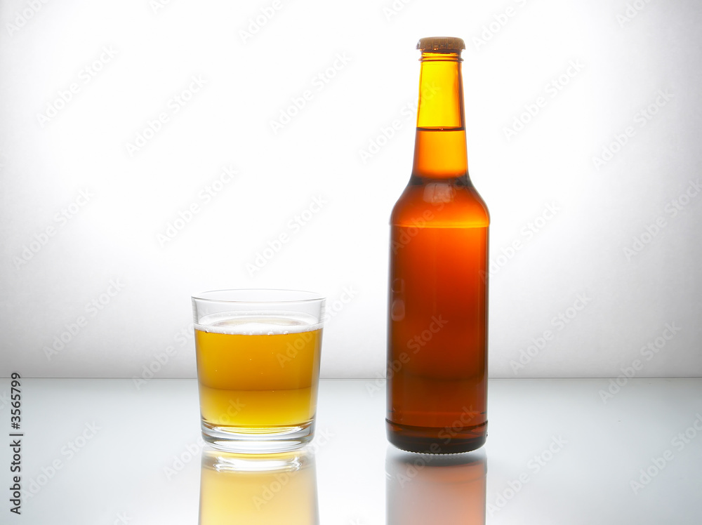 Bottle with beer and a glass on a white reflecting surface