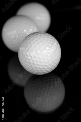 Three white golf balls reflected on black surface.