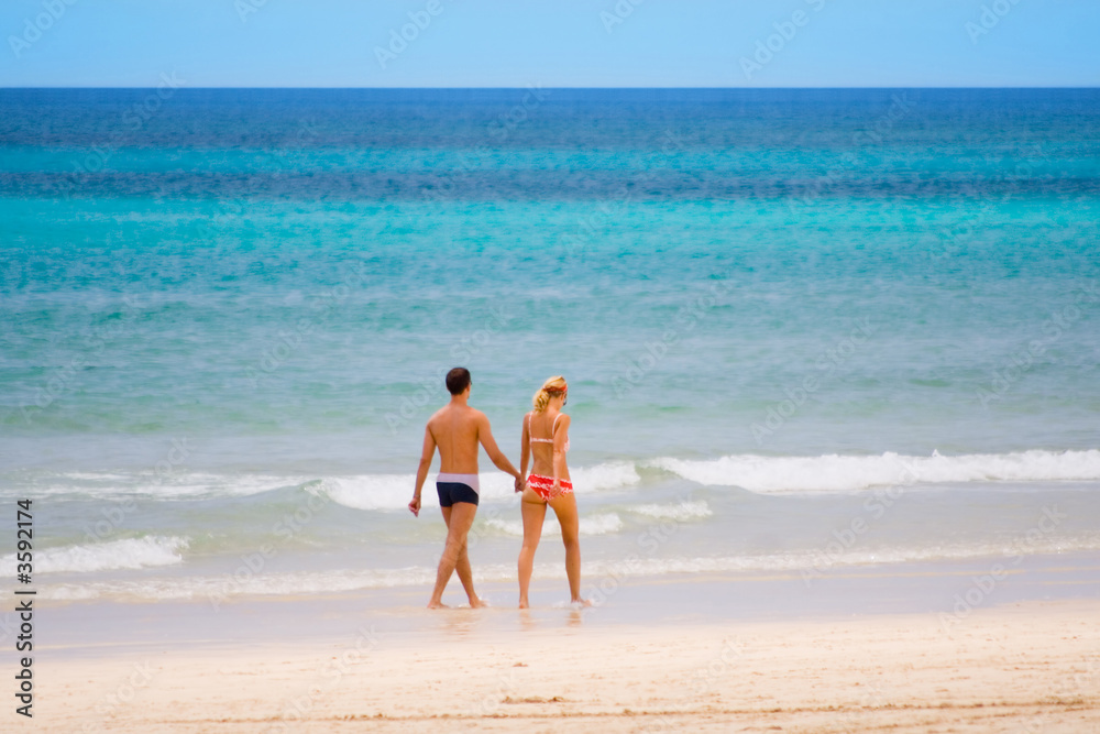 junges paar in badekleidung geht am strand entlang junges paar in badekleidung geht am strand entlang