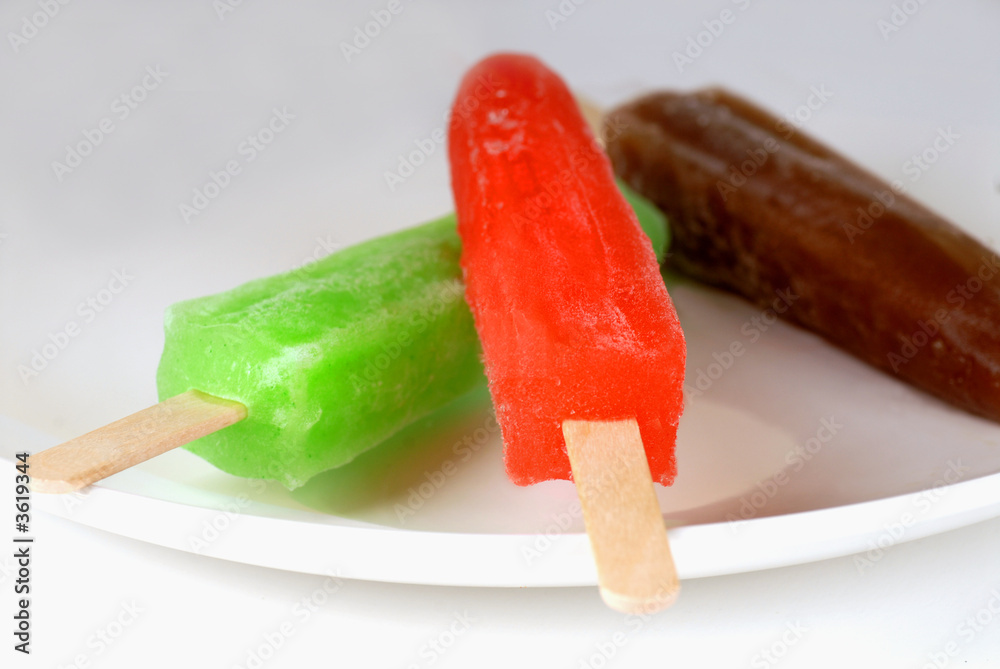 Lime, Cherry and Root beer popsicles on a white plate