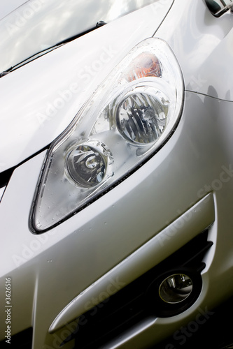 Hood of modern car after rain with drops on a headlight.