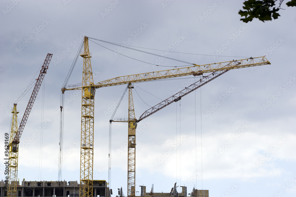 Three cranes in process of work over cloudy sky Three cranes in process of work over cloudy sky