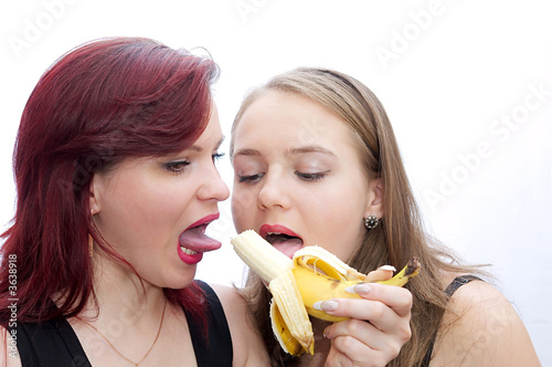 Two girls bite a banana