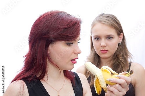 Two girls bite a banana