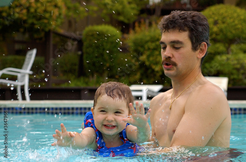 A father and a toddler daughter have fun in the swimming pool