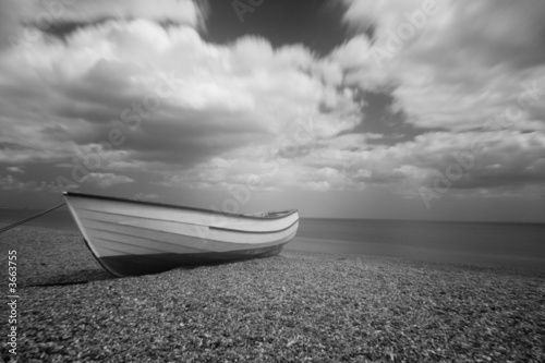 Slika na platnu Open boat on a shingle beach in Suffolk UK. Mono Infrared image.