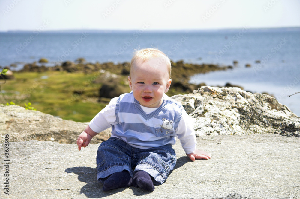 Cute boy sitting on a rock in front of the ocean Cute boy sitting on a rock in front of the ocean