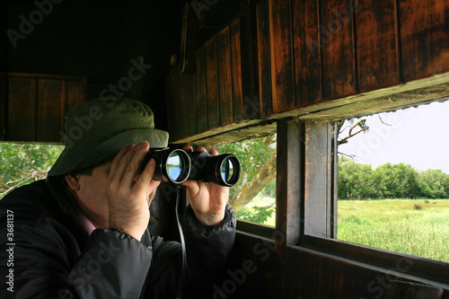 Man looking through binoculars in a birdwatching hideout photo