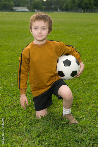 Boy with soccer ball kneeling on a green field © TRITOOTH