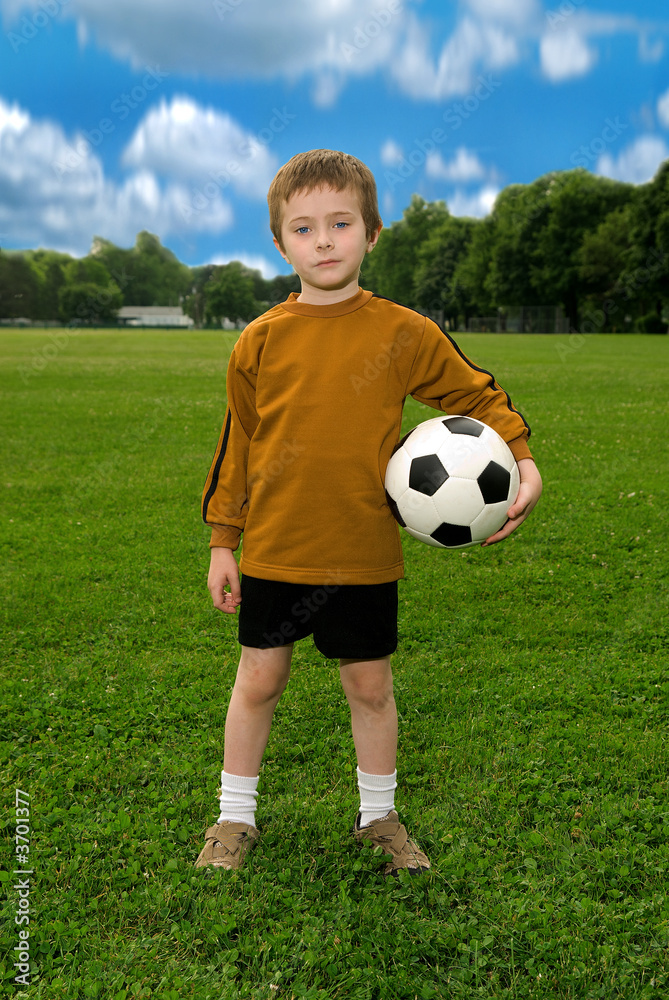 Boy with soccer ball against blue sky and green field