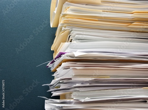 Pile of paperwork against a textured green cubicle wall
