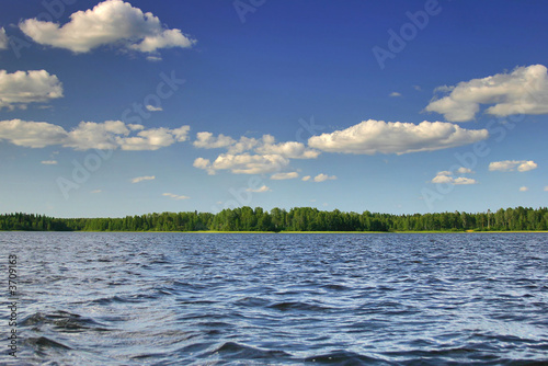Landscape with blue sky, clouds, forest and lake