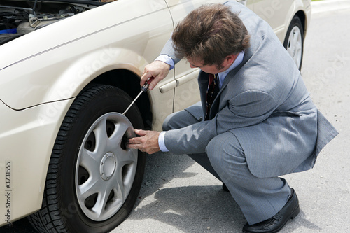 A businessman prying off the hubcap of his flat tire. photo