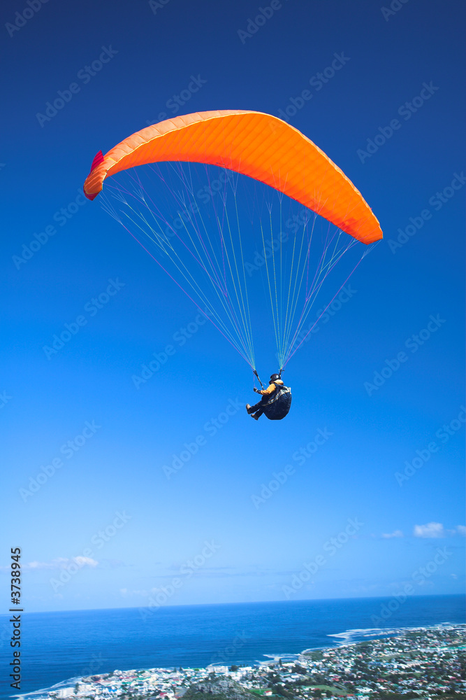 Paraglider launching from the ridge with an orange canopy Paraglider launching from the ridge with an orange canopy