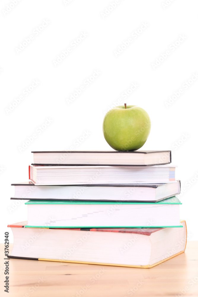 stack of books and green apple on desk - isolated on white
