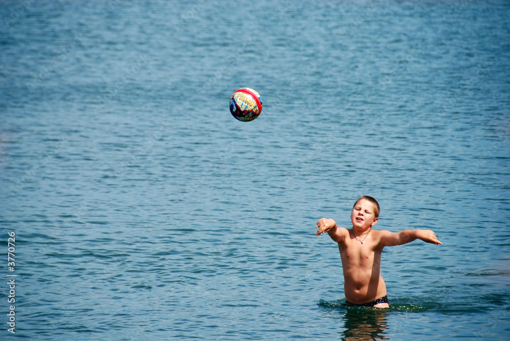 A boy playing with a ball in water