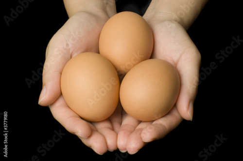 Hands holding three eggs isolated on black background..