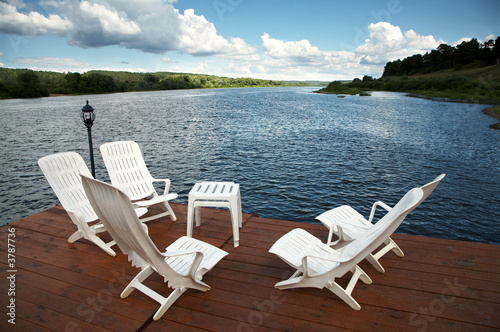 Five white armchairs and table on coast of a reservoir © terex