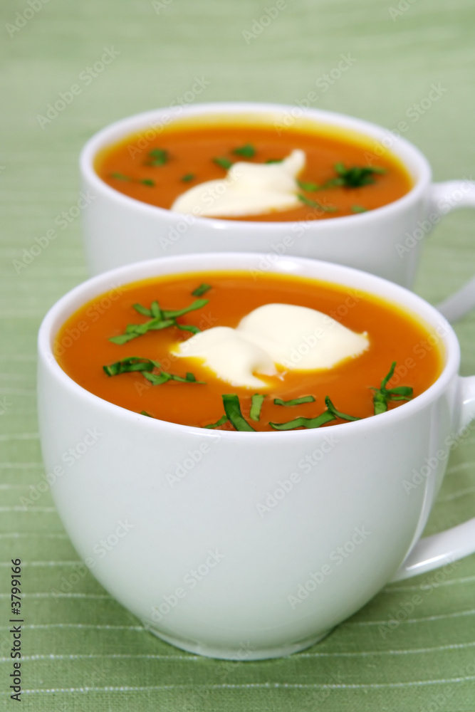 Fresh pumpkin soup in white cups, on green background.