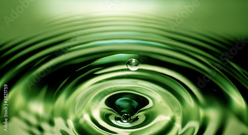 single water drop about to splash into a green pool of water below that already has ripples on its surface