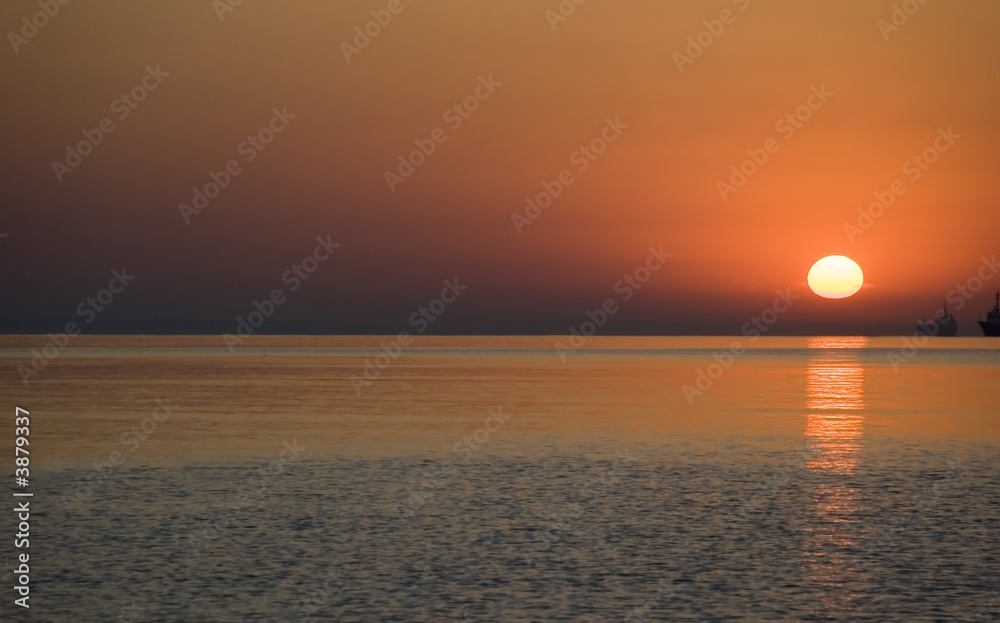 Red sunrise above ocean. With the military ships on a background