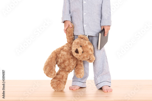 boy in pijama with his teddy bear and book isolated on white