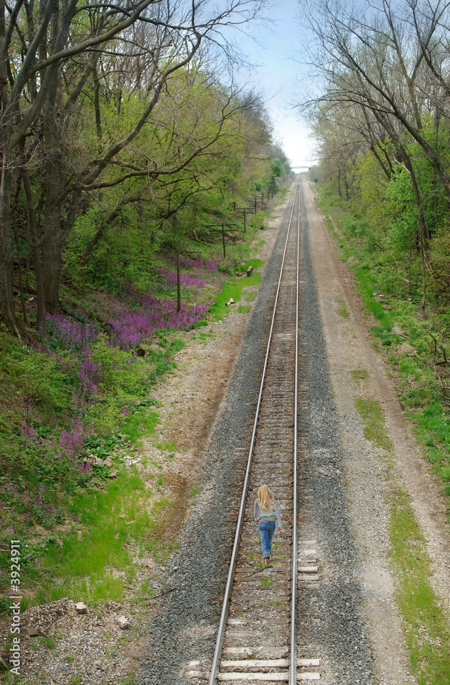 Obraz premium Woman walking on train tracks near the woods.