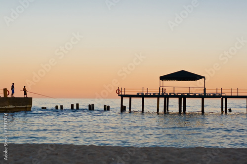 Sundown on sea. Two fisherman on pier