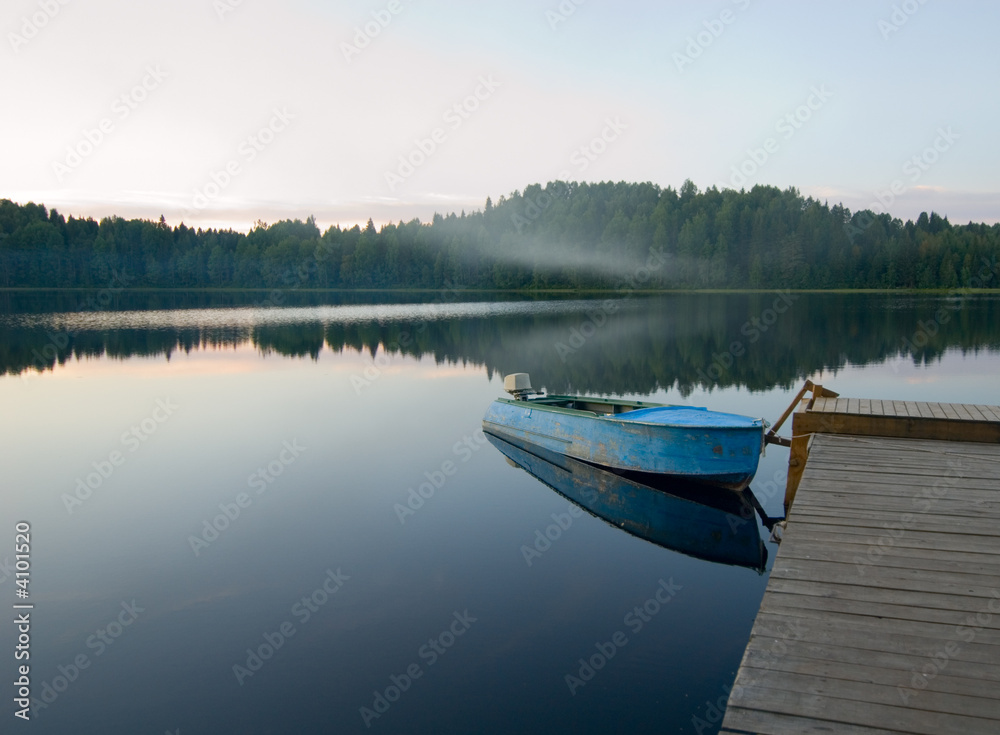 boat reflecting in calm waters of forest lake