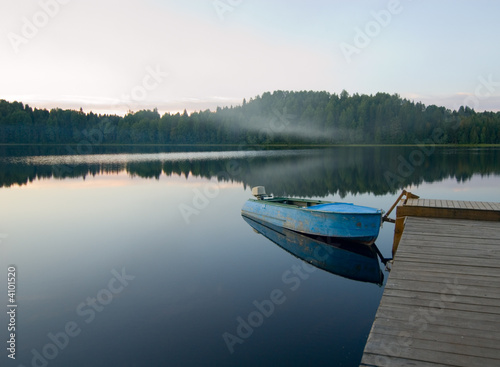 boat reflecting in calm waters of forest lake