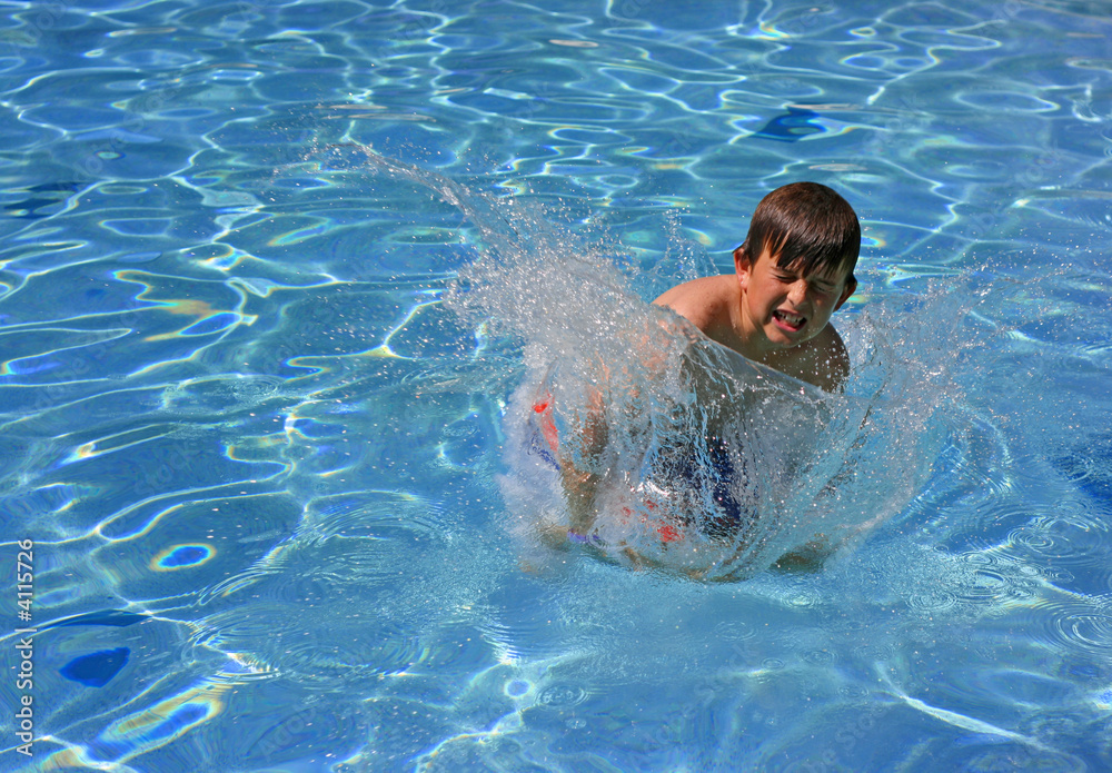 A young boy jumping and splashing into a swimming pool