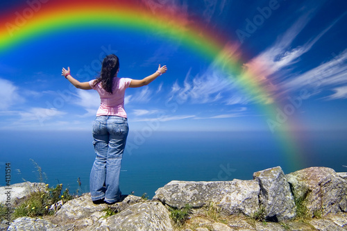 young woman with arms wide open contemplating the rainbow over t photo