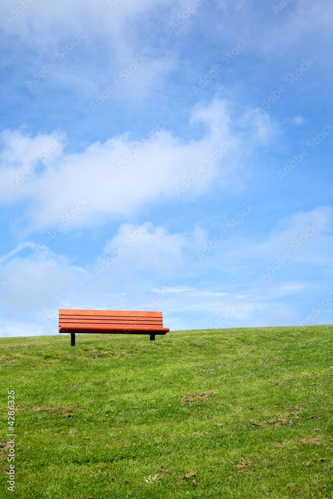 A park bench with a big blue sky and green grass. A park bench with a big blue sky and green grass.