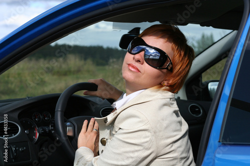 Red-haired woman in sun glasses in a blue car