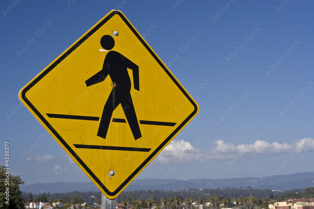 A US pedestrian crossing sign (weathered), against a blue sky. A US pedestrian crossing sign (weathered), against a blue sky.