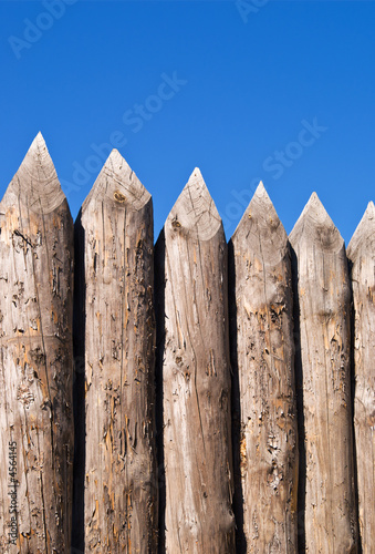 High wall of old wooden sharpened logs over blue sky