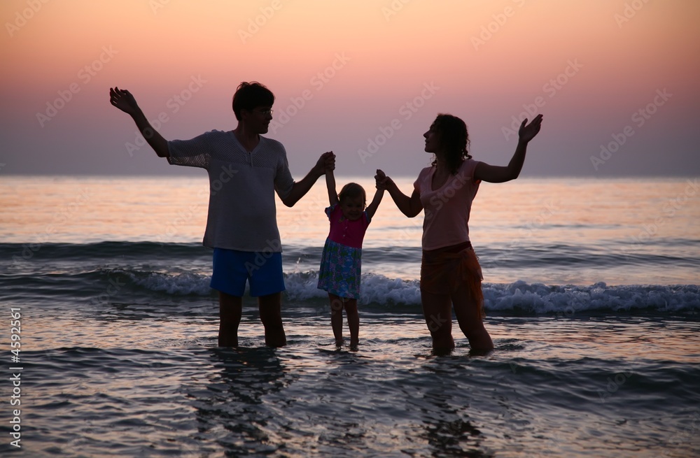 Fototapeta premium Father with mother hold child in sea on sunset