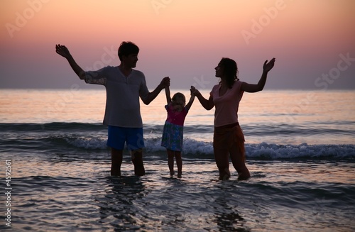 Father with mother hold child in sea on sunset