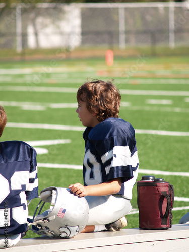 young football player on sideline bench watching action on field Stock