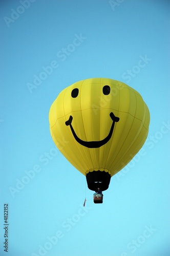 Big yellow happy face hot air balloon against bright blue sky