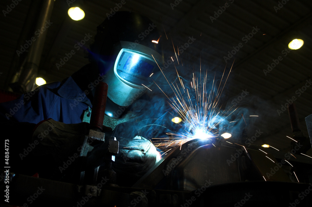 Welder welding a metal part in an industrial environment - obrazy, fototapety, plakaty 