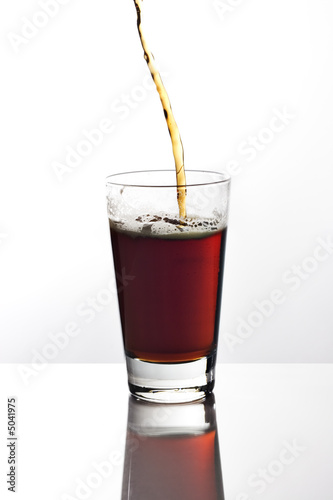 Pouring a glass of dark beer on reflective tabletop