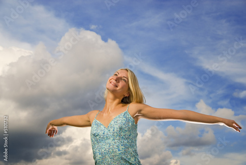 Beautiful blond girl with arms wide open over blue cloudy sky