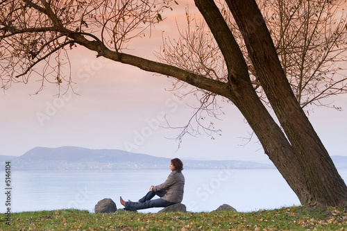 A young woman / lady is sitting and have a relax under a tree