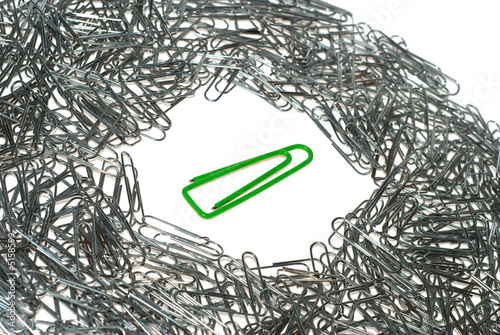 Big isolated green macro paper clip surrounded by many little