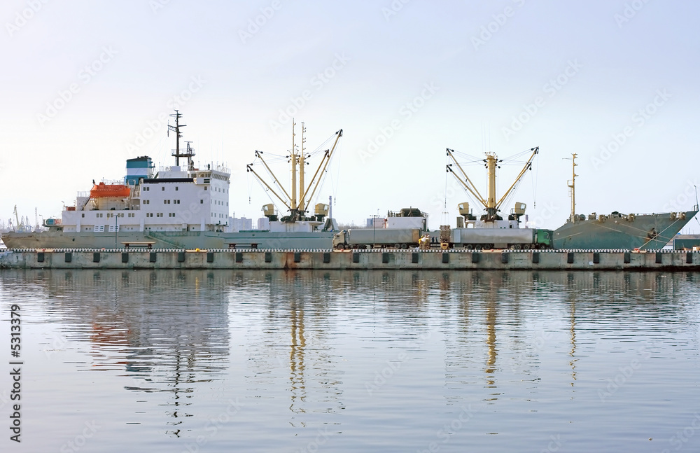 Fototapeta premium cargo ship docked and loading in port fully reflected in water