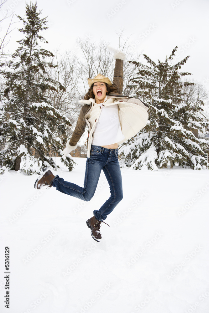 Female leaping into the air in snow wearing straw hat.