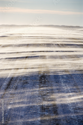 Ice covered road with snow being blown over. © iofoto