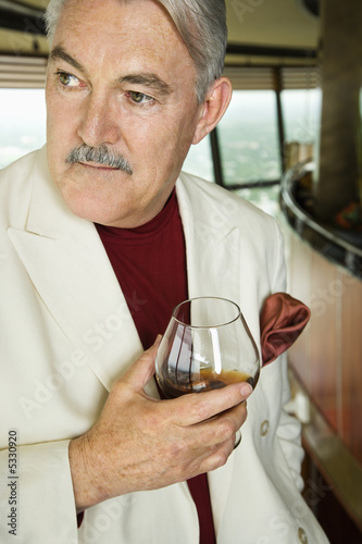 Mature Caucasian man in suit holding snifter of brandy.