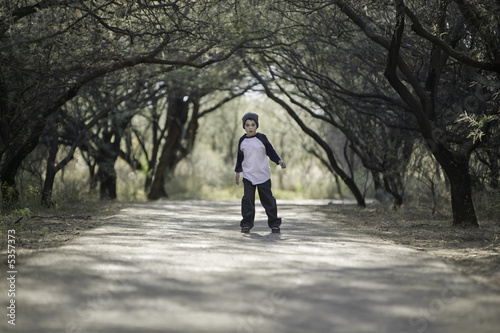 Young boy with a knit cap stopped on a tree-lined path